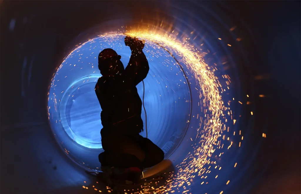 Worker performing metal grinding inside large pipe during fabrication services